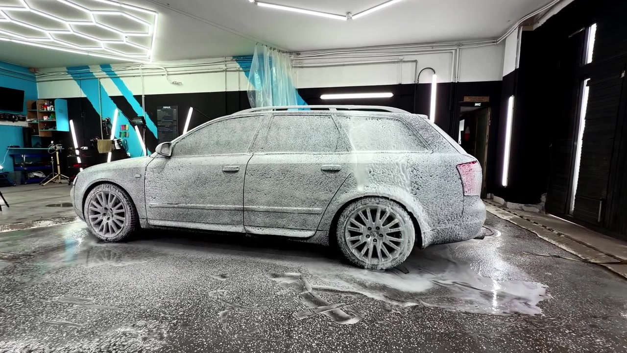 La schiuma copre un'auto parcheggiata durante un lavaggio in un ambiente di garage moderno e ben illuminato.