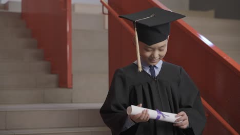 happy asian preschool male student in cap and gown holding diploma and celebrating his graduation