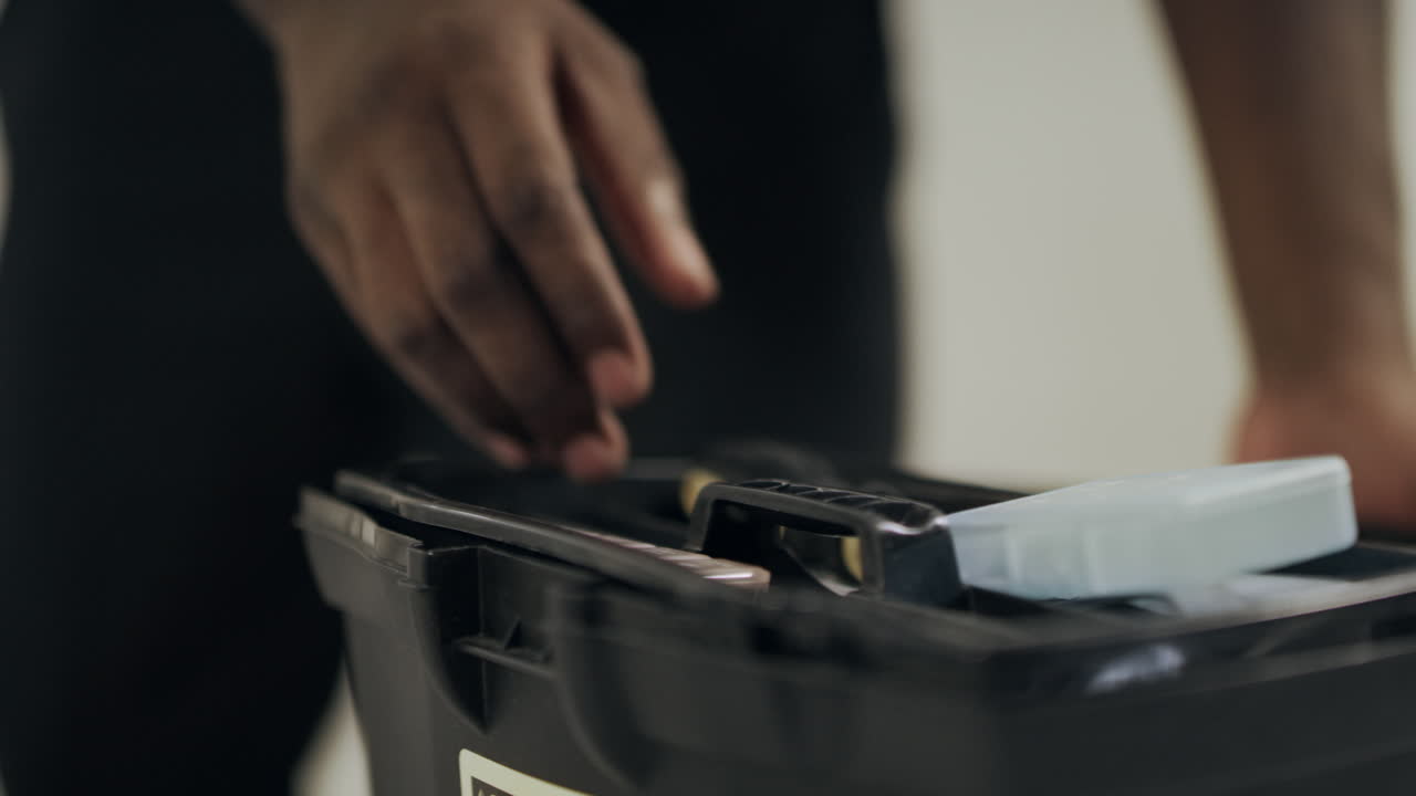 흑인 남자의 손이 도구 상자를 열고 클로즈업 남자의 손이 스크루드라이버를 잡고 있습니다.