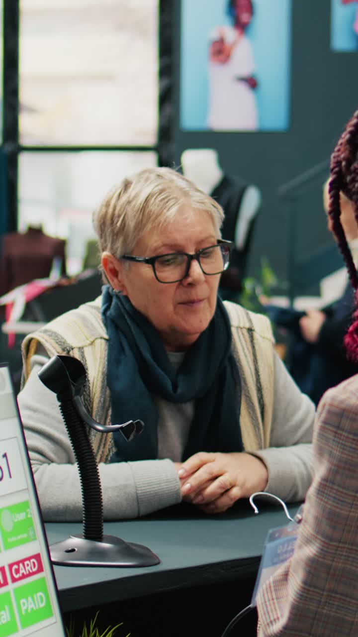 Vertical Video Elderly woman choosing clothing items to by from showroom