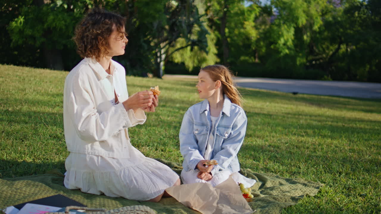Happy family eat snacks on nature. Woman kid enjoying croissant on green lawn