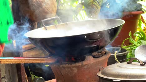metal pan boiling coconut milk over firewood with thick smoke and flame. perfect for traditional cooking, rural food prep, and cultural documentaries