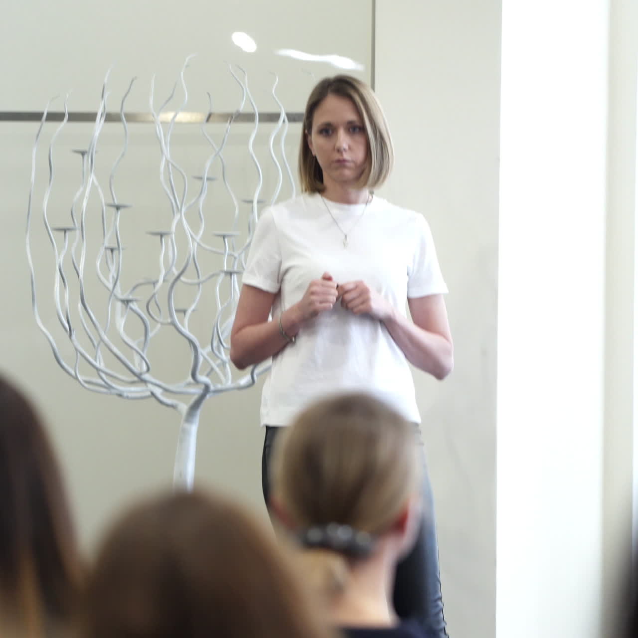 Woman coach speaker tells speech at conference. Young educator explaining something to the auditorium. Public audience listening presentation indoors.