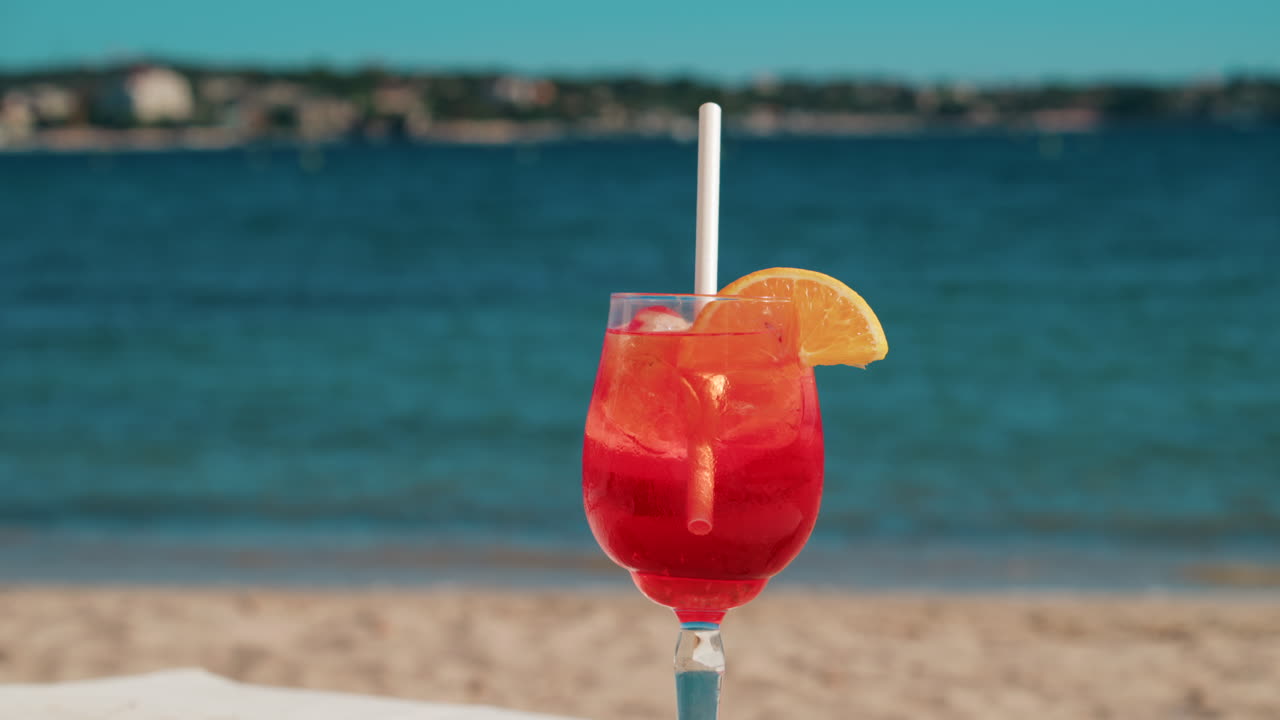 Un cocktail rinfrescante rosso-arancio con ghiaccio e fetta d'arancia sullo sfondo del blu intenso del Mar Mediterraneo