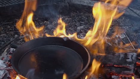 large iron skillet is placed directly onto flames of outdoor bonfire