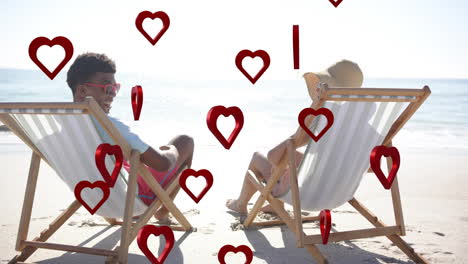 animation of hearts moving over diverse couple in love in deckchairs on beach in summer