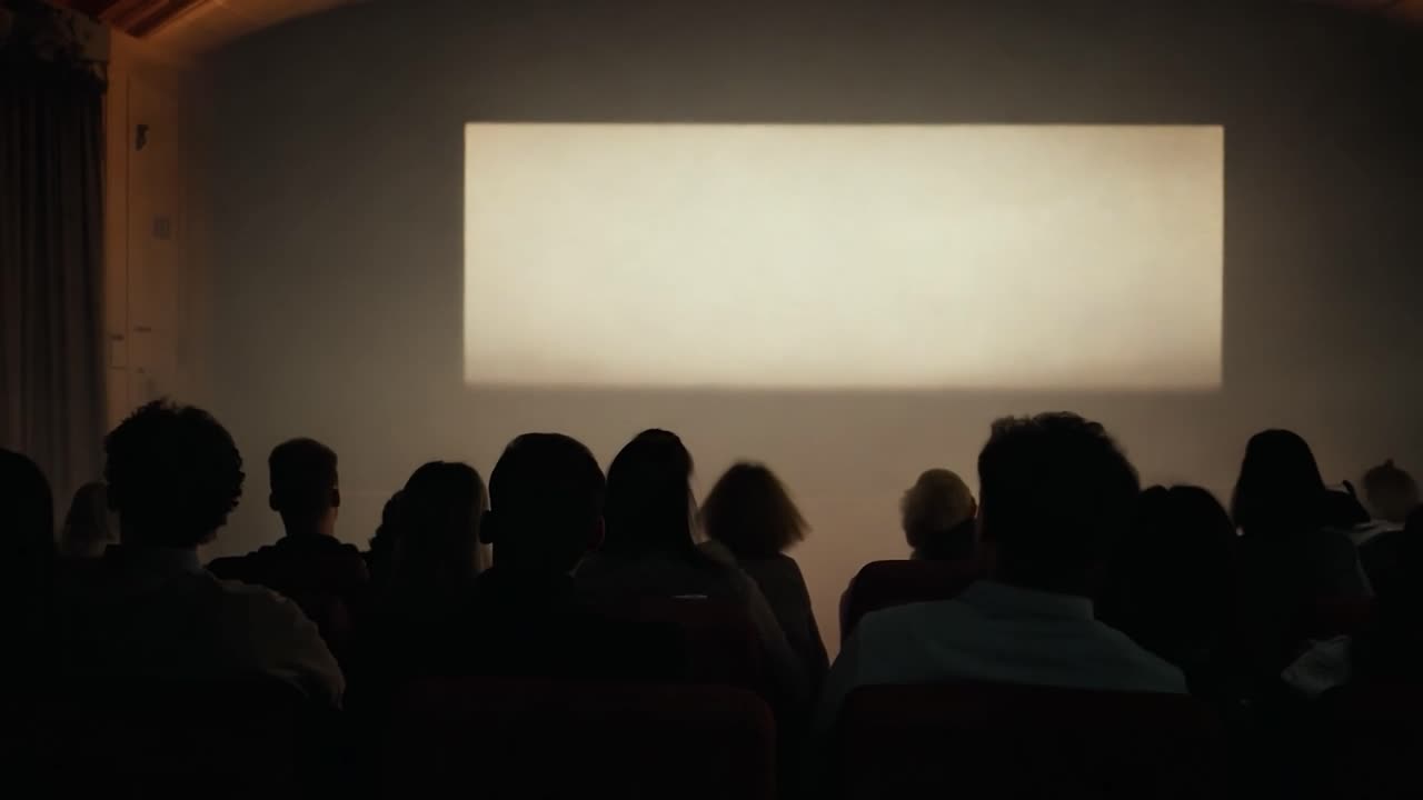 Audience members sit in a dark theater, focused on a bright, blank movie screen, creating an atmosphere of anticipation
