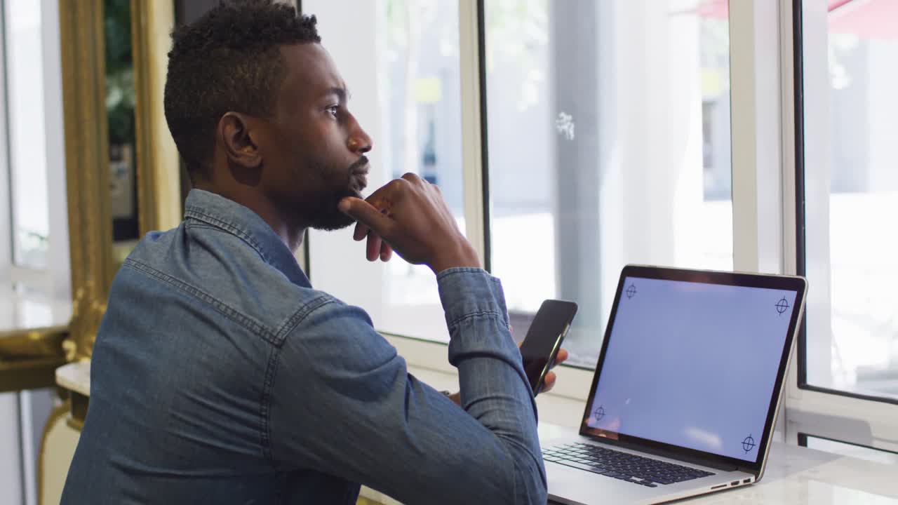 African american businessman using smartphone and laptop in cafe