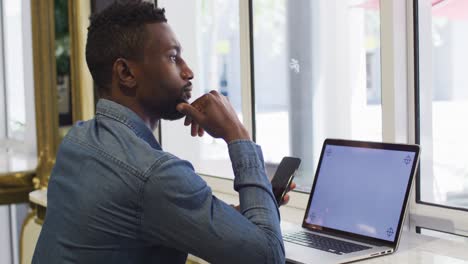 african american businessman using smartphone and laptop in cafe