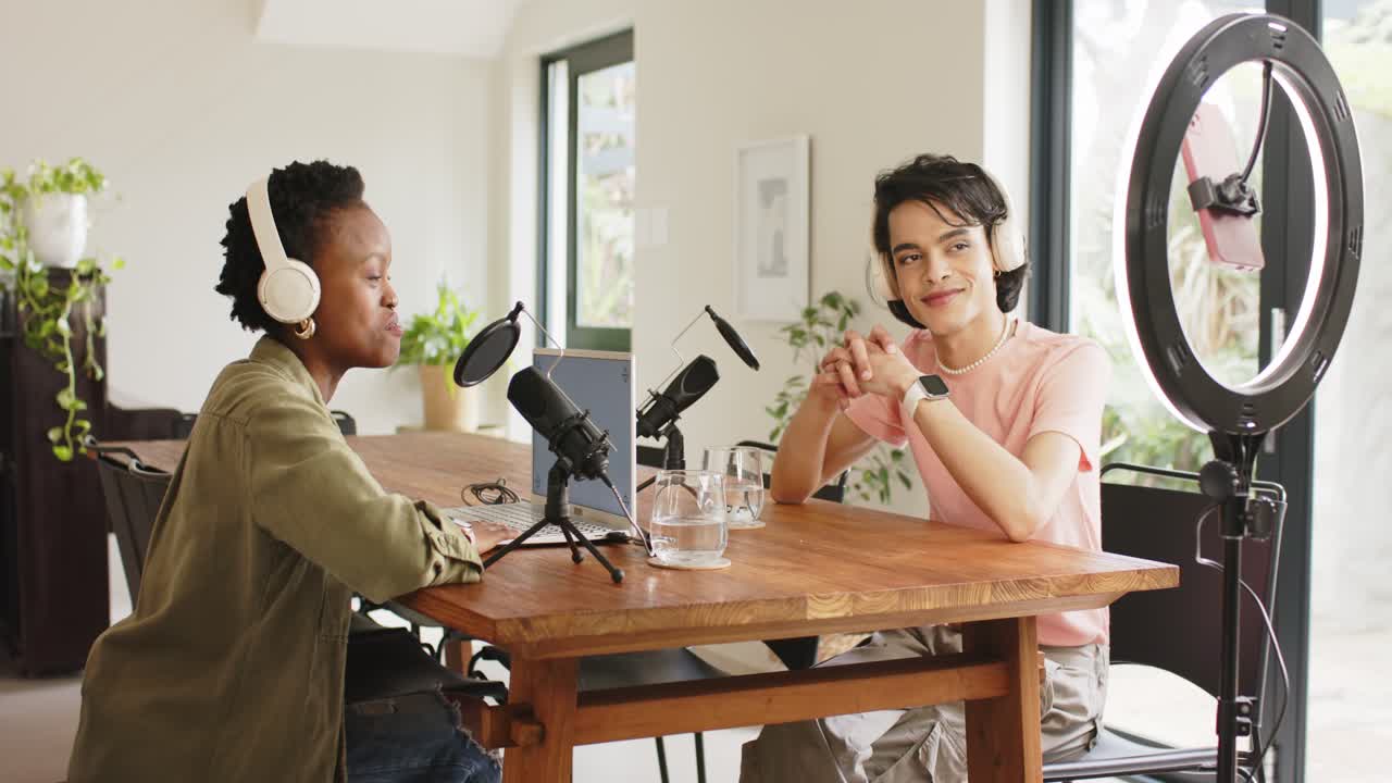 Durante la configurazione di un podcast, colleghi di diverse etnie si chinano a parlare nel microfono e annuiscono alla scrivania di casa.