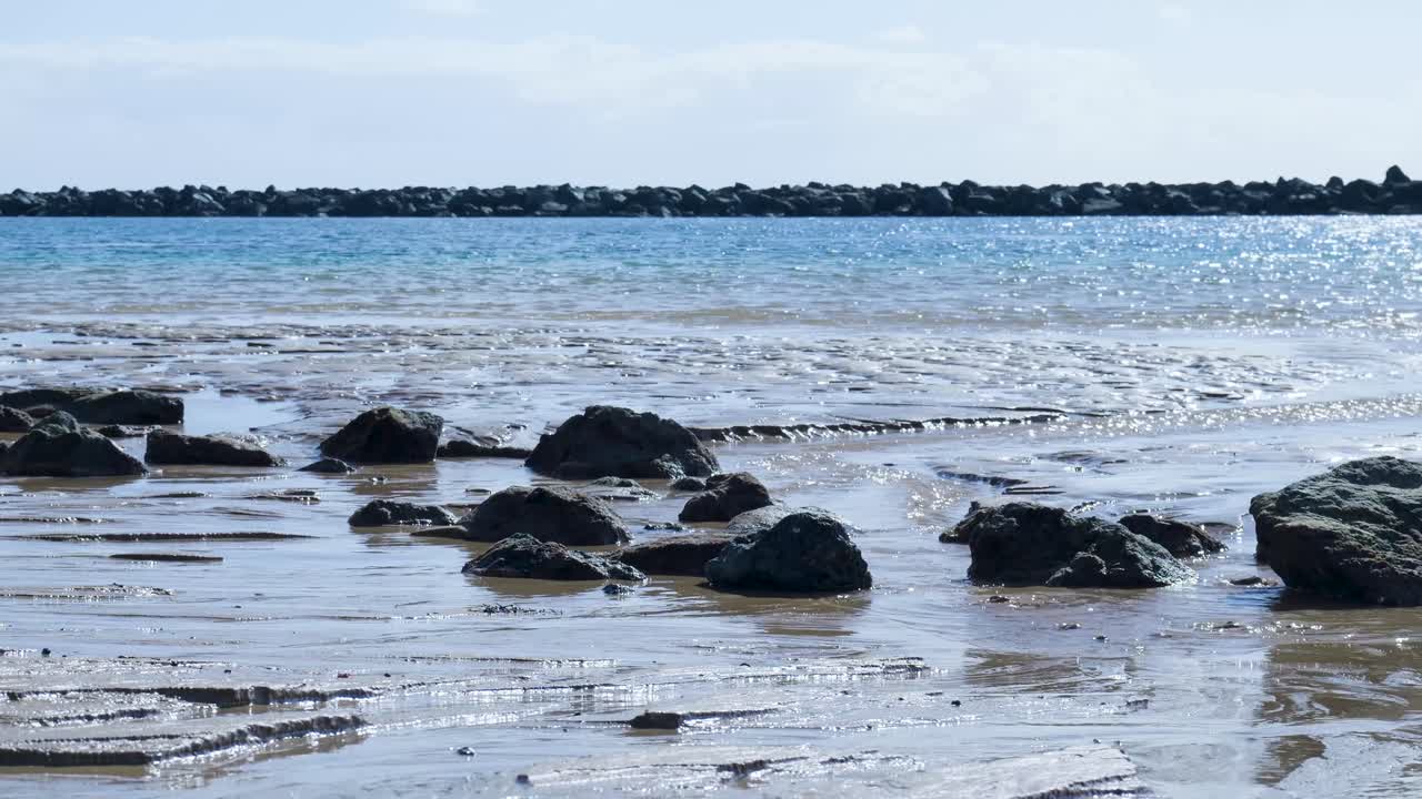 Havvand strømmer omkring sten på en sandstrand ved ebbe
