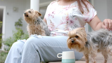 happy plus size biracial woman sitting in garden petting her dogs, slow motion