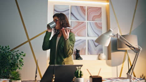 una chica gerente hablando por altavoz bebiendo café en la oficina. una mujer relajada, jefa.