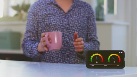 Close-up-of-woman-with-drink-picking-up-smart-energy-meter-measuring-electricity-and-gas-use-at-home---shot-in-slow-motion