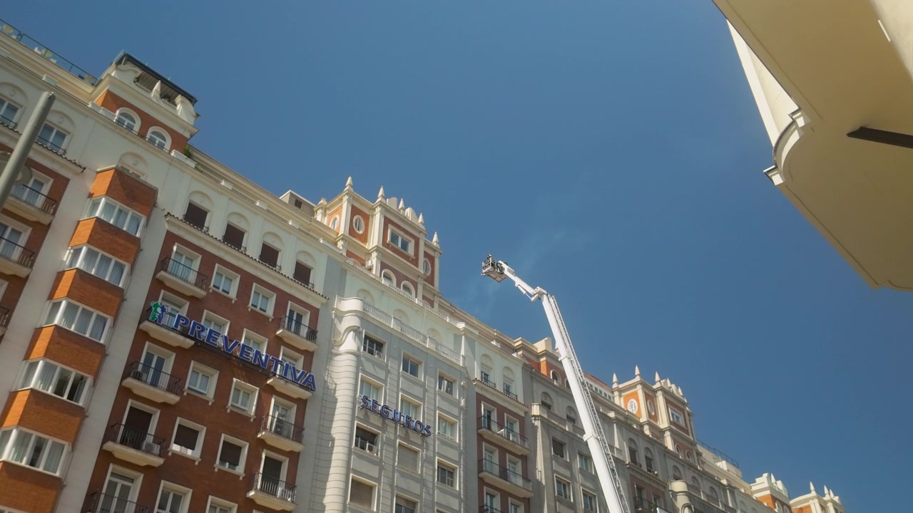 Un'inquadratura dal basso di edifici storici a Madrid, Spagna, con una piattaforma aerea contro un cielo azzurro limpido. Utile per temi di sviluppo urbano e manutenzione della città.