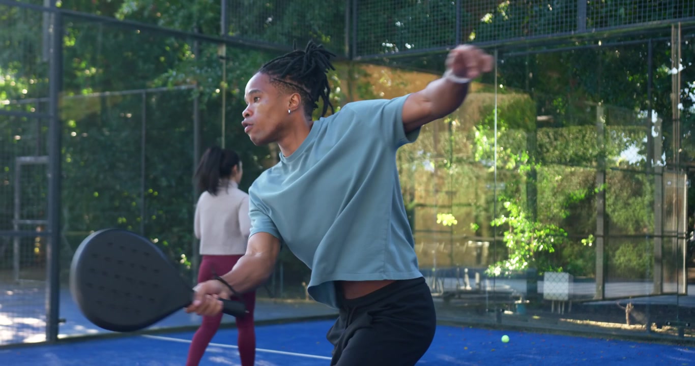 Afroamerikansk par, mann følger ballen, svinger forhånds-racketen på en blå padelbane, returnerer