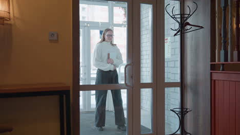 woman seen through glass door entering restaurant while holding bag in hand during daytime with visible modern indoor setting and natural light from outside