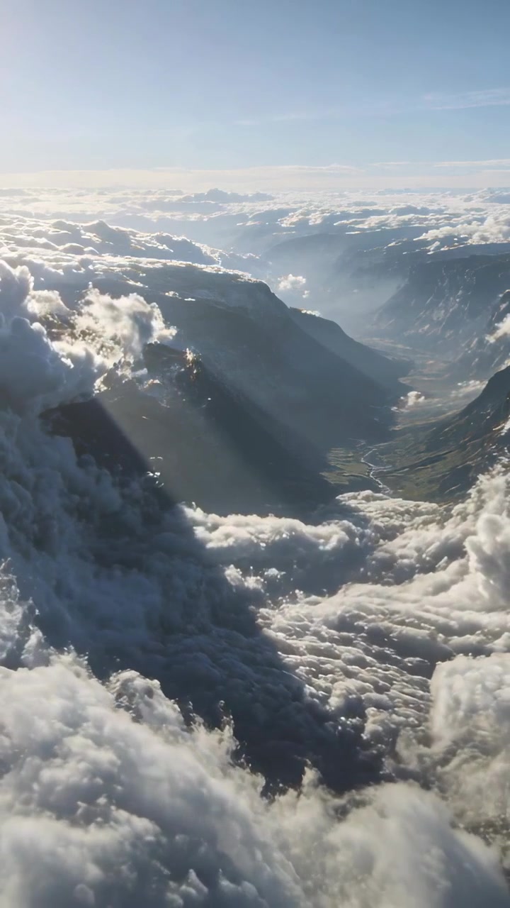 Vidéo verticale : Drone décollant au-dessus des nuages, planant dans une vallée alpine, révélant des rayons de soleil et une rivière