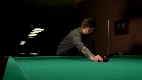 a brutal man with tattoos on his hands is playing russian billiards in a bar.