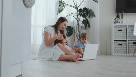 Moderne-Wohnung-Mutter-Und-Zwei-Söhne-Sitzen-Auf-Dem-Boden-Im-Wohnzimmer-Und-Schauen-Auf-Den-Laptop-Bildschirm