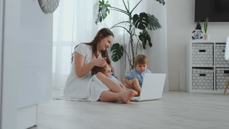 madre apartamento moderno y dos hijos sentados en el suelo en la sala de estar miran la pantalla del portátil