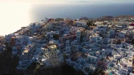 Oia with white cave houses and villas top down view from drone rising during sunset in Santorini, Greece.