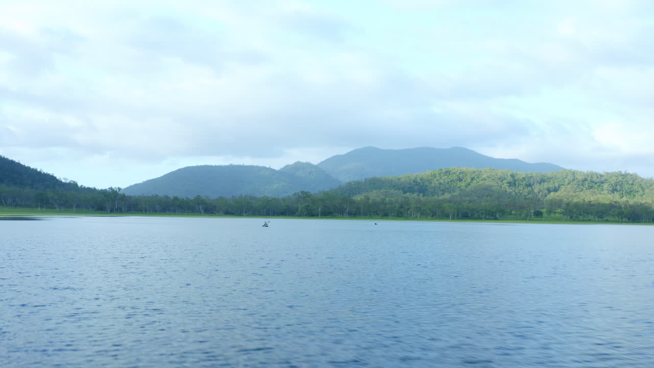 산과 나무로 둘러싸인 댐에서 카약을 타는 어부, 공중 드론 4k