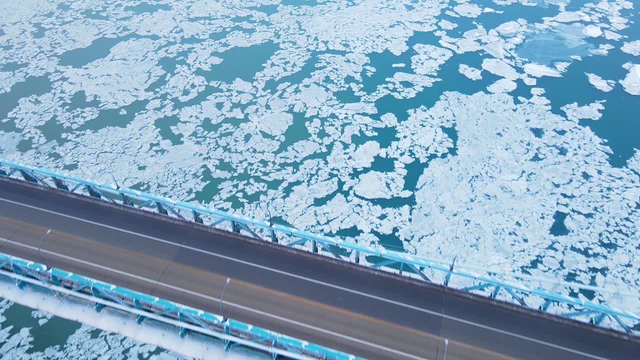 Close-up aerial of Ambassador Bridge deck over ice-covered Detroit river
