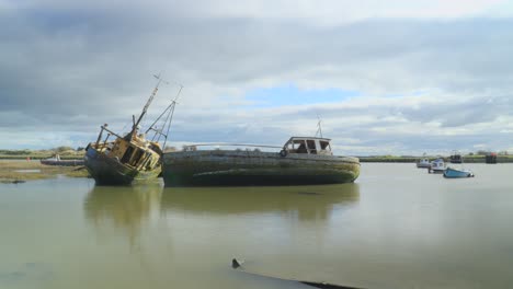 Fishing-boat-shipwrecks-and-smaller-boats-moving-on-receding-tide-as-thick-cloud-moves-across-the-frame