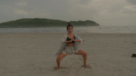 una mujer practica una mezcla armoniosa de ejercicio y yoga en la playa, específicamente haciendo sentadillas profundas