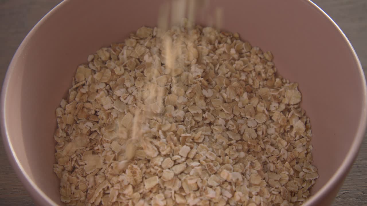 copos de avena que se vierten en un tazón rosa comida para el desayuno por la mañana