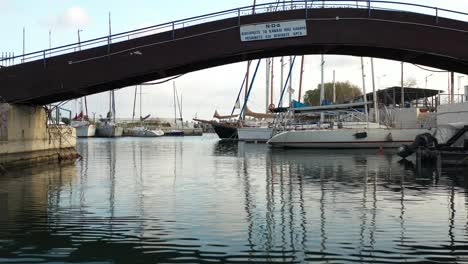 forward drone shot passing under a footbridge with a beautiful yacht and sailing boat on a background