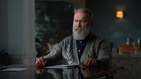 Thoughtful-senior-man-sitting-at-table-with-documents-in-luxury-home-interior