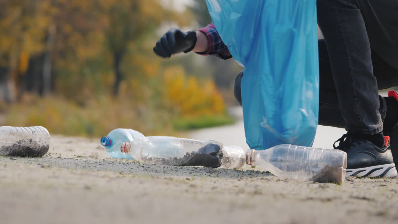 Un uomo con i guanti raccoglie rifiuti di plastica sulla spiaggia e li mette in un sacco. Raccolta di rifiuti e ambiente