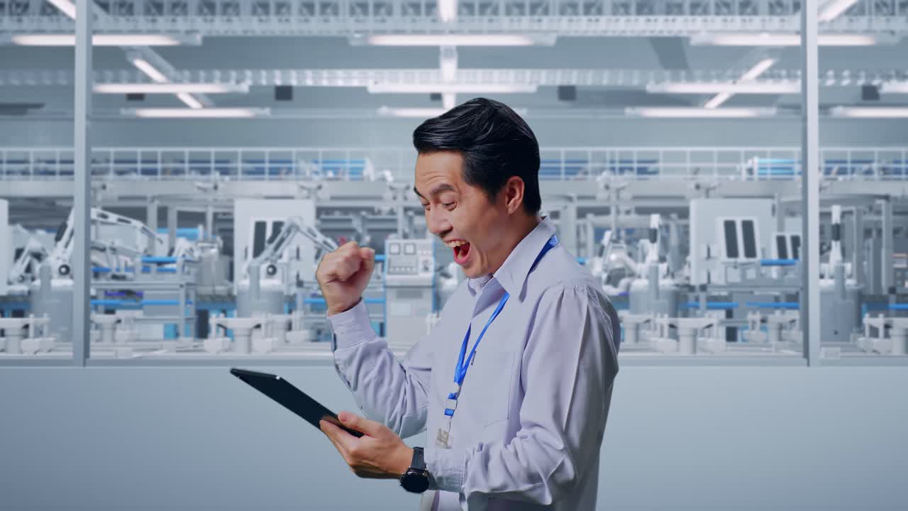 Side View Of An Asian Male Professional Worker Standing With His Tablet At Factory Digitalization, He Raises His Fist Up With Screaming Goal After Check On The Tablet