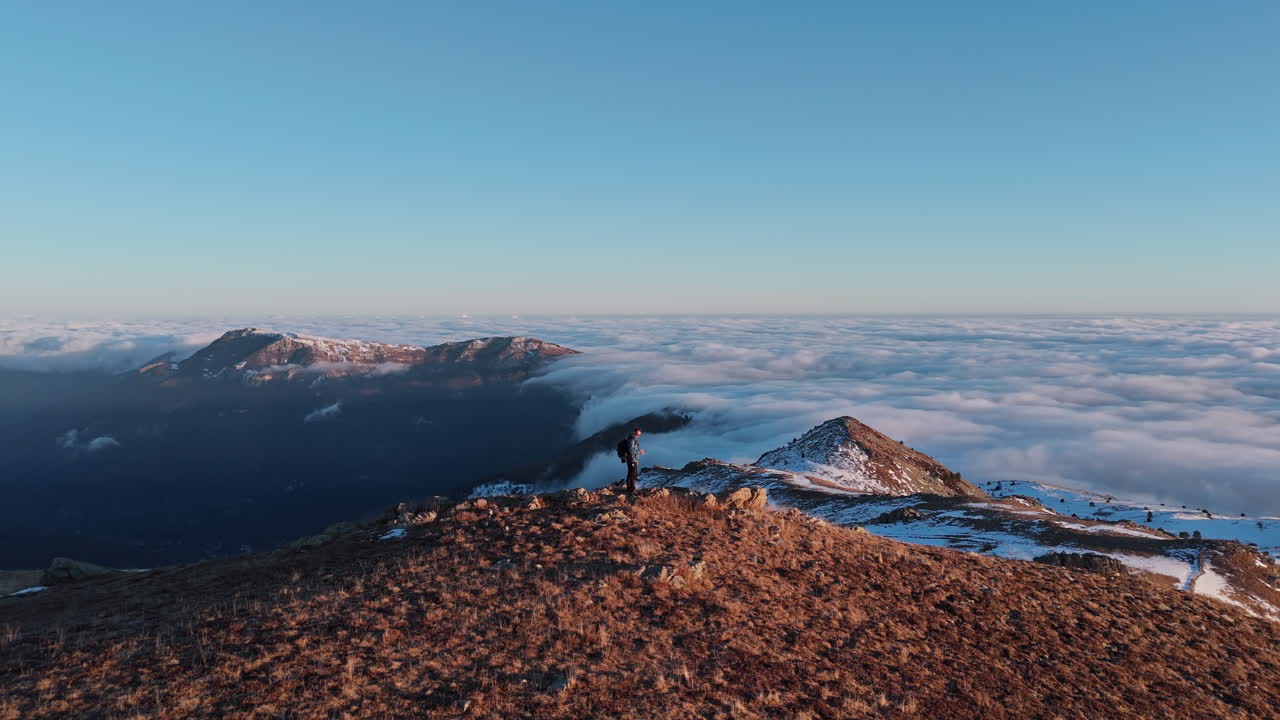 Un escursionista sta su una cima di montagna con una vista mozzafiato sulle nuvole all'alba