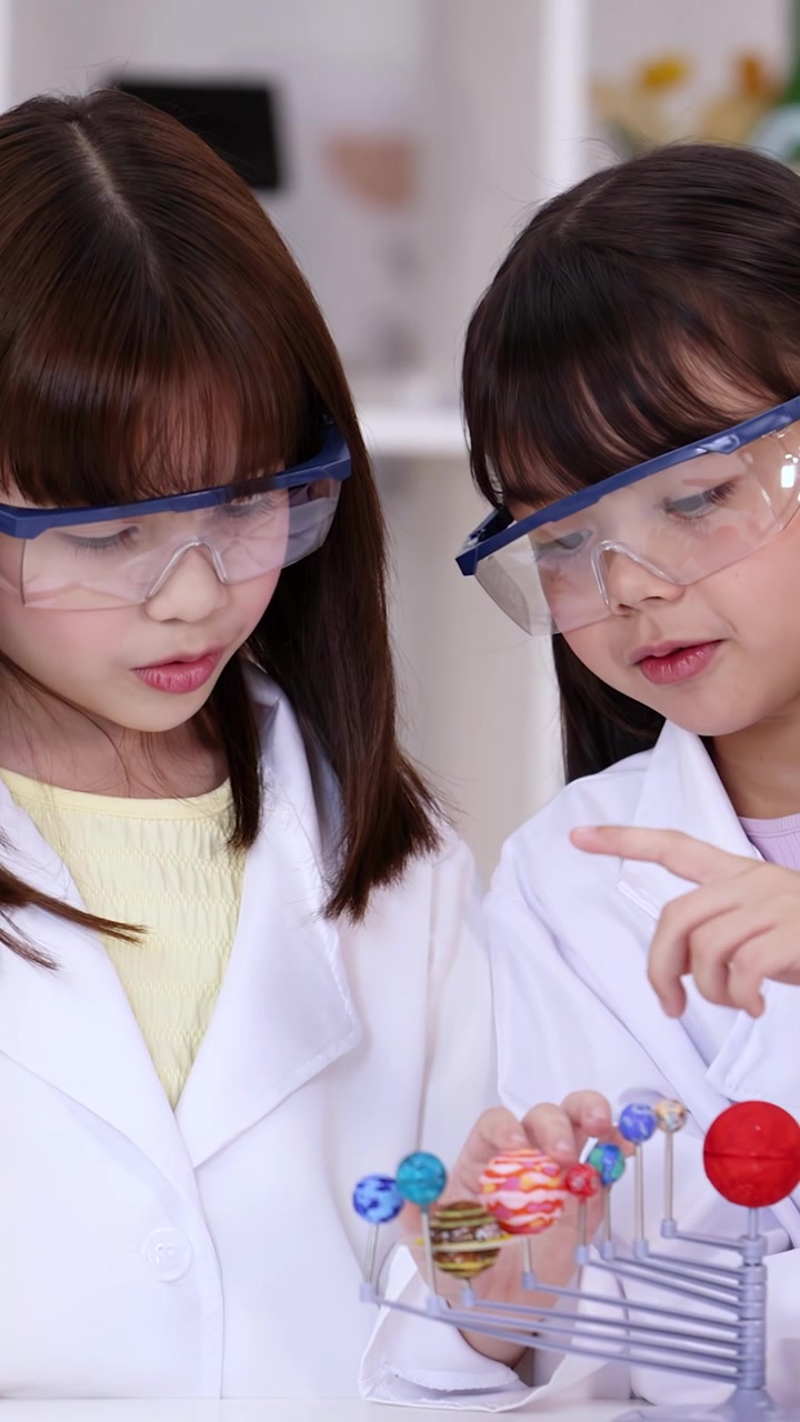 Two Young Girls in Lab Coats Learning About the Solar System