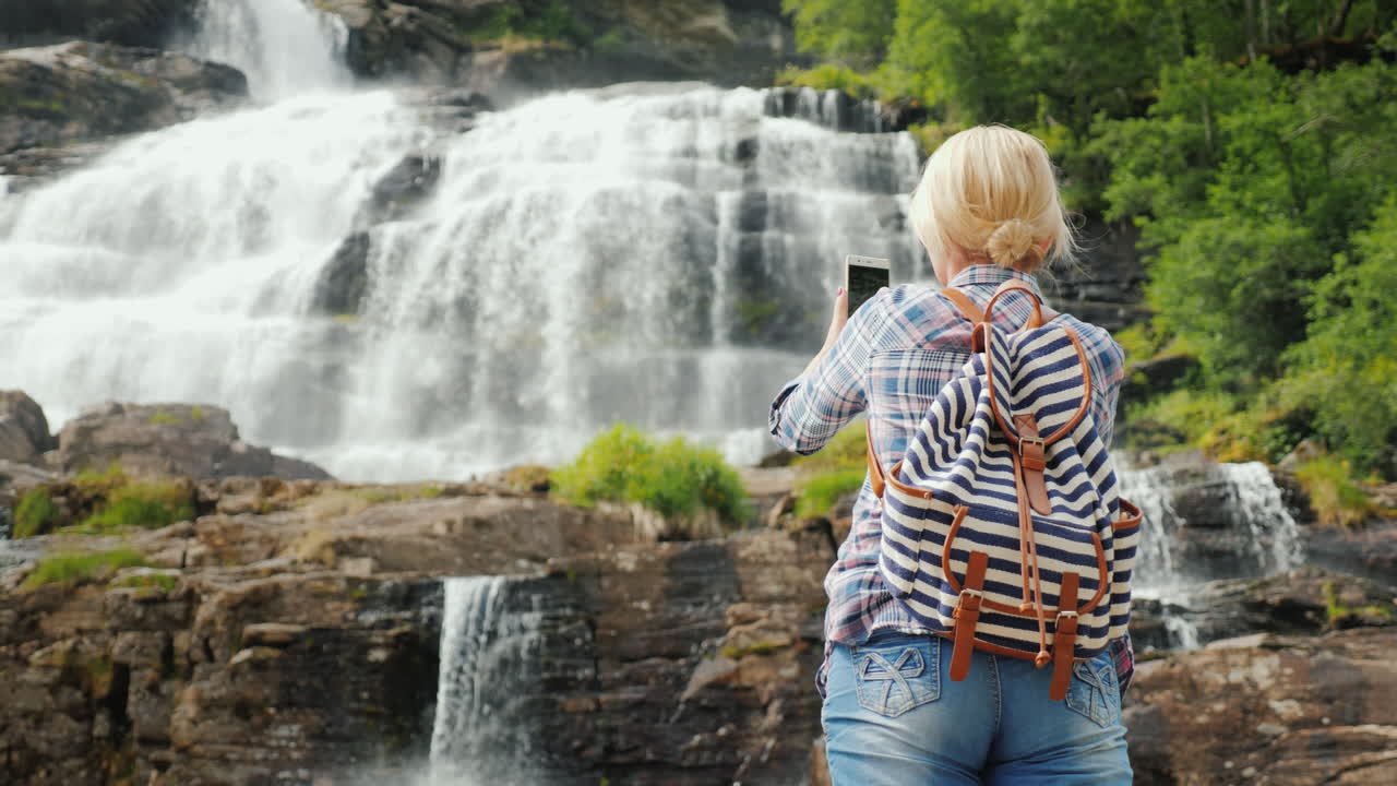 una joven fotografía una pintoresca cascada de tvindefossen en noruega - un viaje a escandinavia y