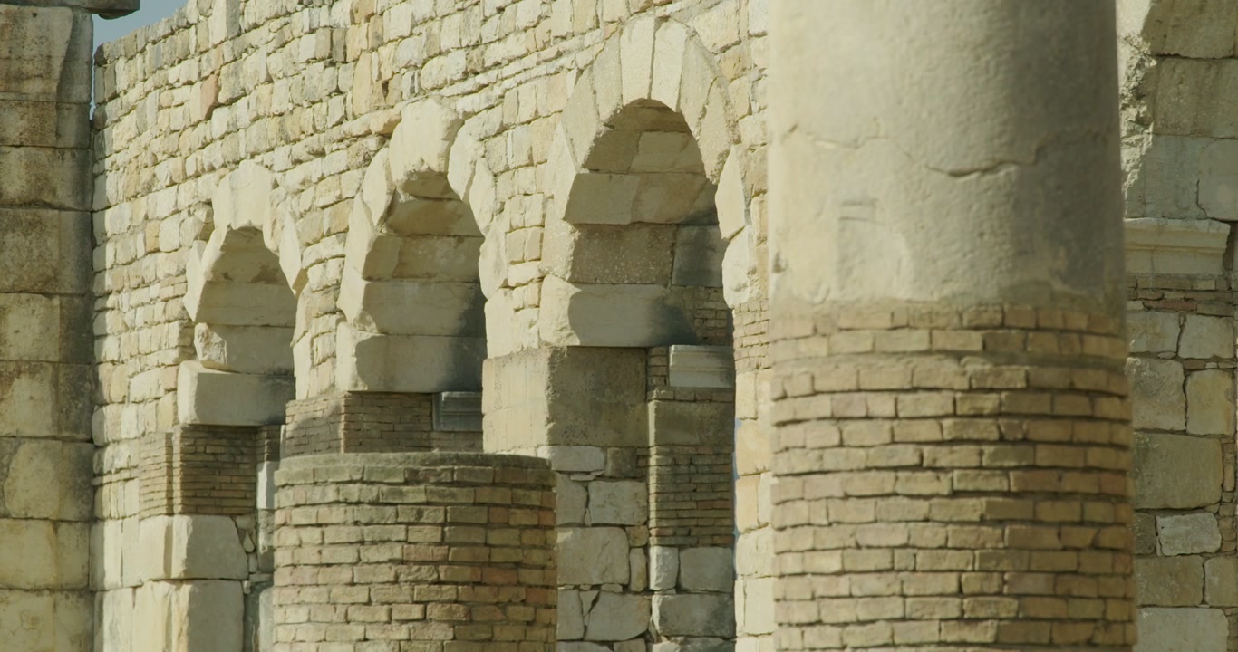 Primo piano cinematografico a livello del suolo della Basilica di Volubilis, che evidenzia archi romani, colonne e muratura conservata che illustrano la raffinatezza architettonica di uno dei più importanti siti romani
