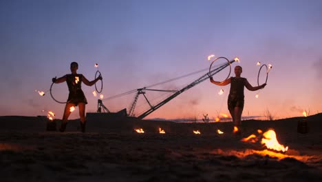 a group of men and woman fire show at night on the sand against the background of fire and tower cranes