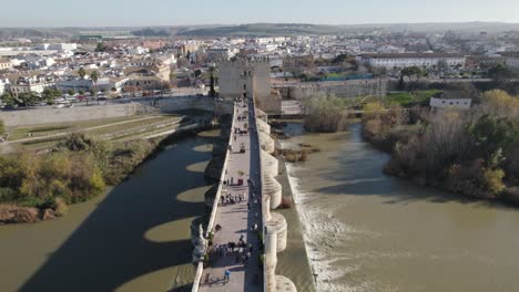 aerial forward view of cordoba old roman bridge over river guadalquivir with people. andalucia, spain