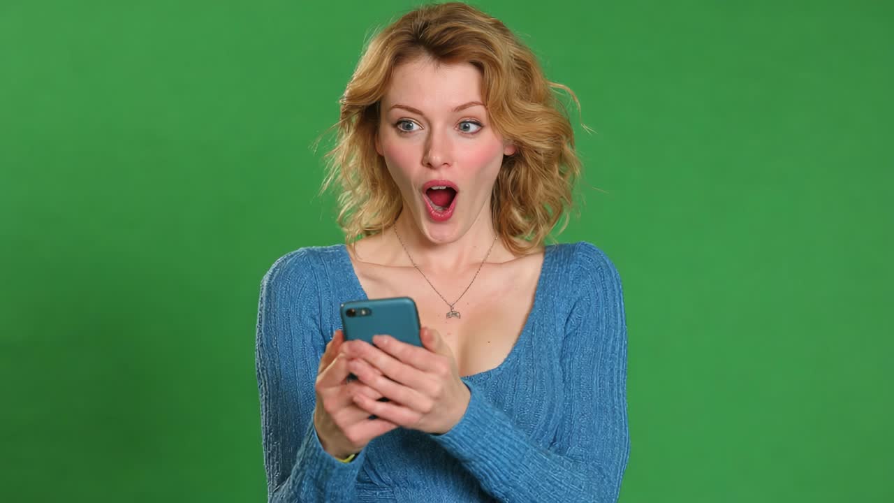 Captivating Surprise: A Young Woman Reacts with Astonishment While Engrossed in Her Smartphone, Showcasing a Range of Emotions on a Vibrant Green Background