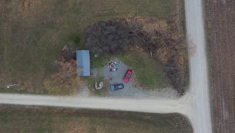 Aerial-top-down-view-of-a-group-of-people-sitting-around-a-fire-in-front-of-Country-house-beside-a-red-car,-shot-by-a-drone-flying-down-on-an-autumn-day-in-rural-Rome,-Pennsylvania