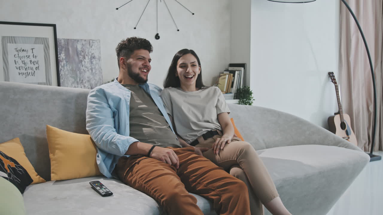 Cheerful Young Couple Laughing While Watching Comedy On TV