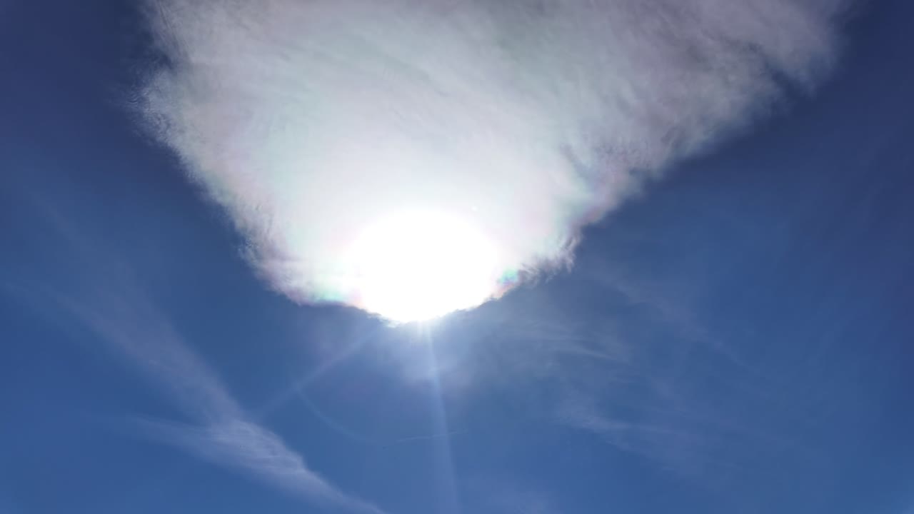 Timelapse of a high-altitude cirrus cloud evolving in a blue sky, with a radiant sun veiled temporary. Low angle shot
