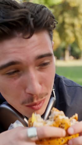 man eating a hamburger in a park