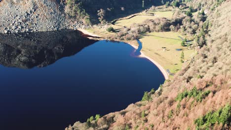 A-rising-aerial-shot-of-the-Guinness-Lake-or-Lough-Tay-Luggala-Wicklow-Ireland-with-calm-glass-like-water-and-reflections-with-the-river-Cloghone-Once-part-of-the-Guinness-Estate