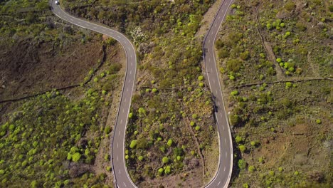 Top-down-aerial-shot-of-U-turn-curvy-road-surrounded-by-patchy-lush-greenery-in-Tenerife,-Canary-Island,-Spain