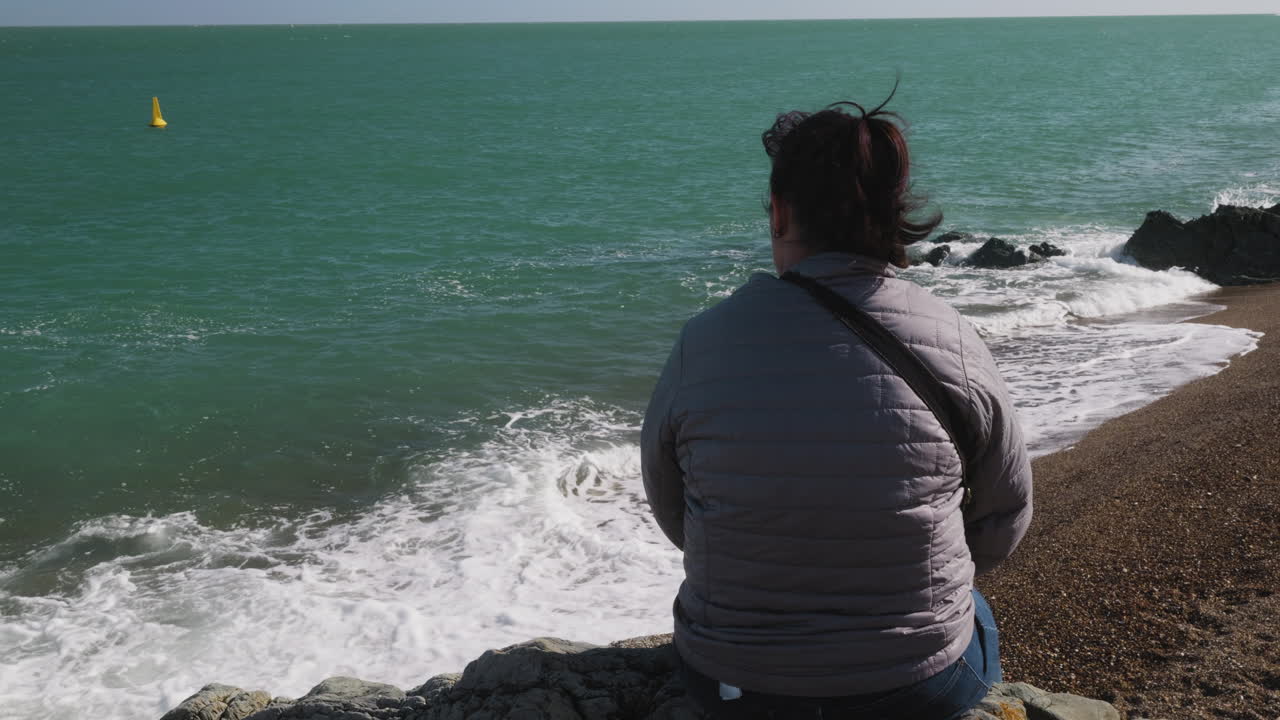 Vista da dietro la spalla di una donna attraente che si rilassa e guarda l'oceano in vacanza, a Greystones, Irlanda.