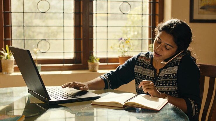 Taking call, woman in kurta typing laptop, writing in notebook with headset at home, copy space